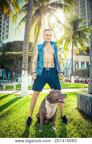Man and dog american pit bull terrier relaxing at the park at sunset. Caucasian male with strong dog