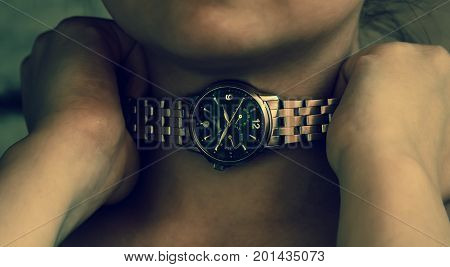 women hands clasp the neck of the watch in an attempt to break the time that suffocates, the part of the chin is visible, two hands are clenched into fists, the iron strap of the clock around the neck