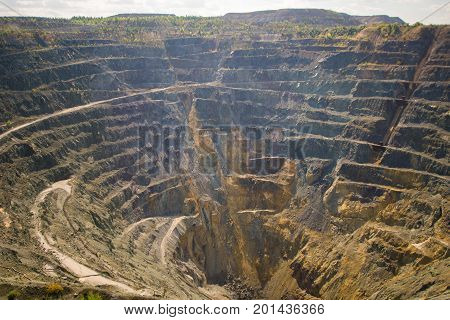 Big Abandoned opencast mining quarry against cloud sky.