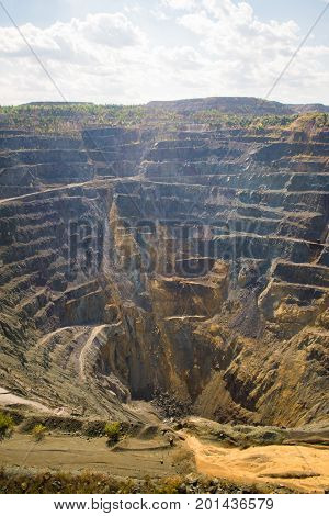 Big Abandoned opencast mining quarry against cloud sky.