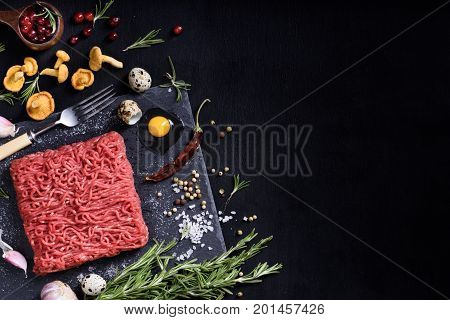 Raw juicy ground meat ready for roasting on a black chalk board background. Fillet with mushrooms herbs pepper and cranberry. Space for text. Above view.