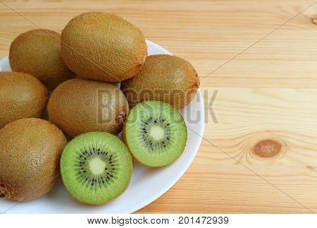 Plate of many fresh ripe whole fruits and cross-sections of kiwi fruits on wooden table, with free space for design and text