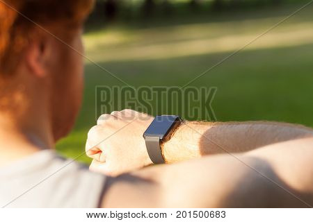 Redhead athlete watching in smart wath or fitness tracker. Summer morning outdoor