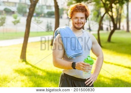 Happiness redhead athlete holing bottle and towl smiling and looking at camera. Outdoor