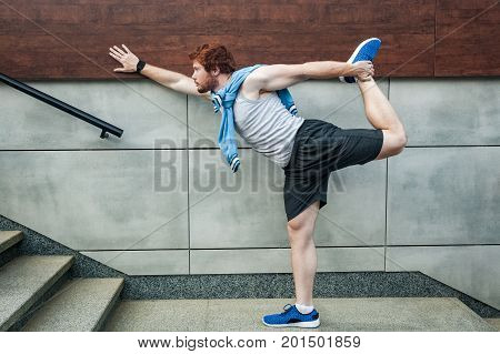 Fitness sport young adult redhead man in sportswear doing yoga fitness exercise in the city street over gray concrete background. Outdoor sports clothing and shoes urban style.