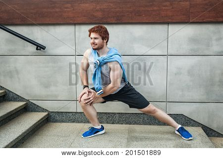 Fitness young man in sportswear doing yoga fitness exercise in the city street over gray concrete background. Outdoor sports clothing and shoes urban style. Lookung at camera and smile. Outdoor shot