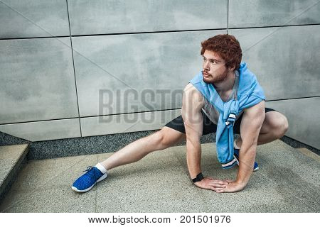 Young adult man in sportswear doing fitness exercise in the city street over gray concrete background. Outdoor sports clothing and shoes urban style. Seriosly looking away. Outdoor shot