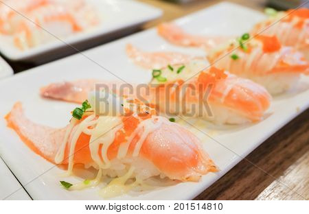 Grilled toro salmon sushi (sake nigiri) with shrimp eggs (tobiko) spring onion and mayonnaise top on rice serve on white plate Japanese food background or texture.