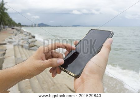 A man using left index finger for texting cellphone on the beach