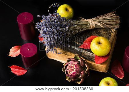 Warm fall composition on black background. Old books, candles, green apples, dry lavender, artishok and red autumn leaves making cozy romantic atmosphere. Copy space