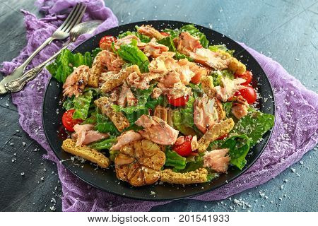 Cesar salad with salmon, cherry tomatoes, garlic, crutons, romaine lettuce and parmesan