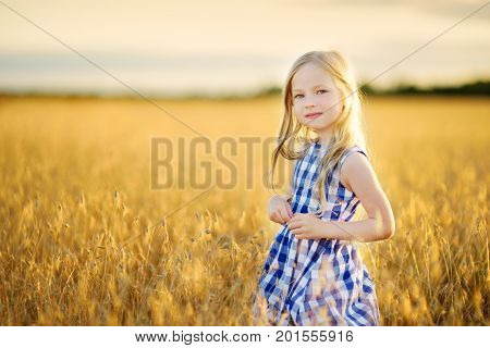 Adorable Girl Walking Happily In Wheat Field On Warm And Sunny Summer Evening