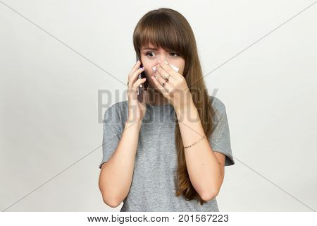 Portrait of a pretty woman having flu. girl blowing nose standing over gray background