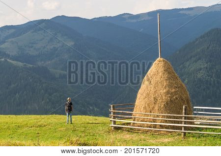 Trekking male hiker standing near haymow on top of carpathian hills and enjoying beautiful sights. Sight of beautiful west ukrainian mountain area in summer at sunset