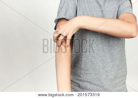 Girl in grey shirt scratching her arm. Scabies. Scratch the hand over gray background