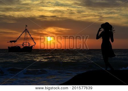 Back view of woman silhouette watching a sail boat at sunrise