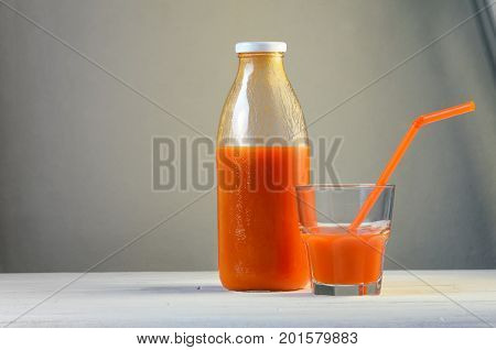 A bottle of carrot juice and a glass of carrot juice with a straw on white wood table. Still life of a healthy eating concept