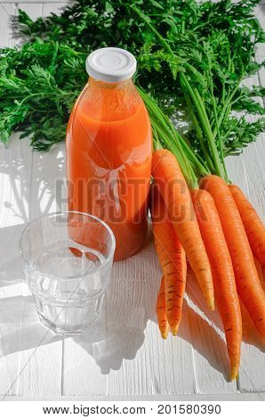 A bottle of carrot juice with empty glass and some fresh carrots on white wood table. Still life of a healthy eating concept
