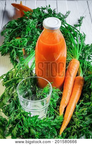 A bottle of carrot juice with empty glass and some fresh carrots on white wood table. Still life of a healthy eating concept