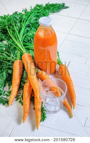 A bottle of carrot juice with empty glass and some fresh carrots on white wood table. Still life of a healthy eating concept