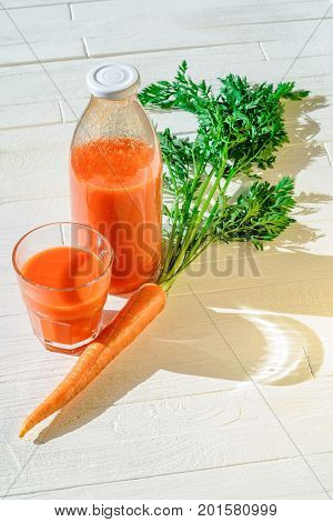 A bottle of carrot juice with with a stuffed glass and one fresh carrots on white wood table. Still life of a healthy eating concept