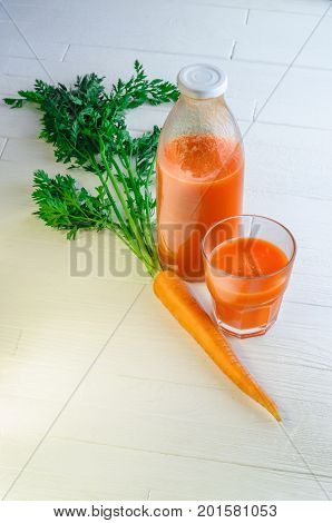 A bottle of carrot juice with with a stuffed glass and one fresh carrots on white wood table. Still life of a healthy eating concept