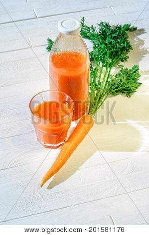 A bottle of carrot juice with with a stuffed glass and one fresh carrots on white wood table. Still life of a healthy eating concept