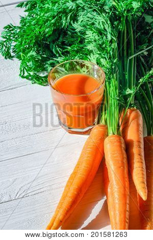 Glass of carrot juice with a bunch of fresh carrots on a white wooden table top view. Still life of a healthy eating concept