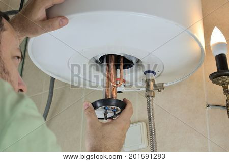 Man's hand putting a new water heater in a boiler