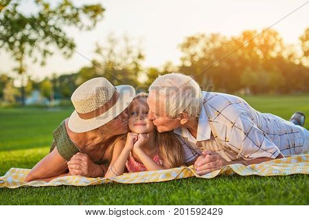 Grandparents kissing granddauther. People lying outdoors. Love to grandchildren.