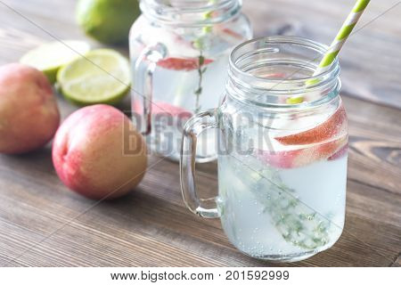 Glass jars of water with fresh lime juice and slices of peach