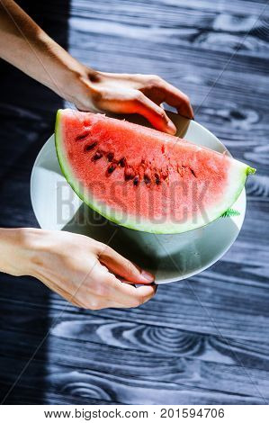 Slice of watermelon on white plate in woman hands ready for eating top view with blurry black wood table background