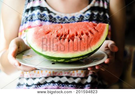 Watermelon background. Girl in a colorful summer shirt holding a plate with a large slice of watermelon in the sun