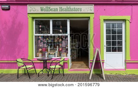 Clifden Ireland - August 4 2017: The pink facade of the small business Wellbean Healthstore with green trim table and chairs outside open door and display window. Street scene.