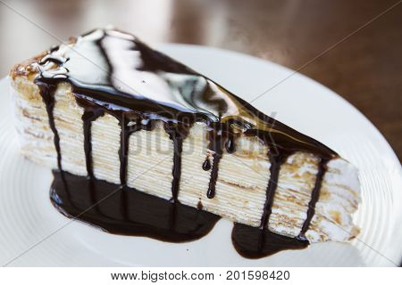 Homemade chocolate cake with cream layer within and topped with rich chocolate shavings.Piece of cake with dark chocolate on a white plate
