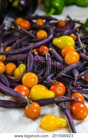 Vertical shallow focus photo of colorful tomatoes purple beans bell peppers and eggplant on a white surface