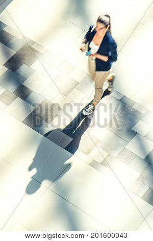 Silhouette of a walking woman with long shadow in a public building hall top view . Abstract background of blur in motion figure of a girl from above. Low speed shutter shot.
