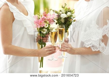 Young brides holding bouquets of beautiful flowers and glasses with champagne on lesbian wedding