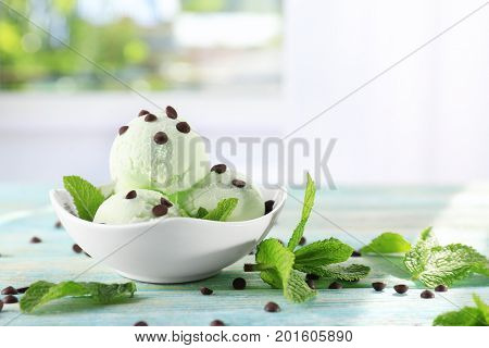 Bowl with delicious mint chocolate chip ice cream and fresh leaves on table