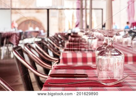 The tables of a street cafe, ready for dinner, with glasses for wine and forks and knives on red chequered tablecloths, and rows of chairs, selective focus, with a place for text