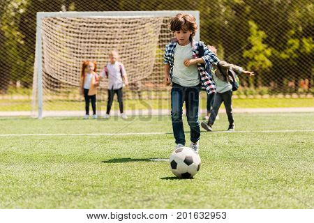 cute little boy running with ball while playing soccer with friends