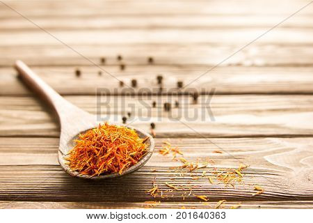 Spice saffron in wooden spoon and pepper on the table. Close-up.