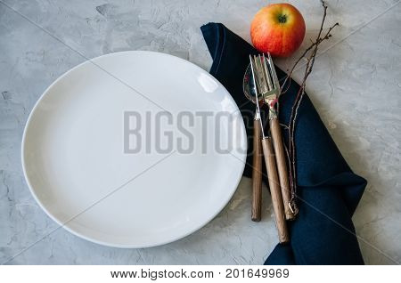 White Round Plate, Red Apple And  Tree Brunches On A Wooden Background. Autumn Holidays Concept.