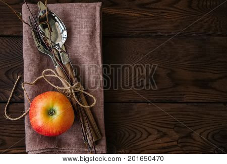 Tree branches, apple, cutlery on a linen sackcloth on a wooden background. Copy space and top view. Autumn mood, Halloween, Thanksgiving, Holiday concept.