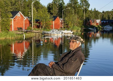KOKKOLA, FINLAND ON JULY 07. View of an old gentleman relax this side boathouses along the channel on July 07, 2017 in Kokkola, Finland. Evening and sunshine. Editorial use.