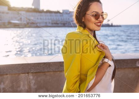 Young stylish woman wearing bright colorful blazer and sunglasses walking on the city street. Casual fashion, fall look. Plus size model.