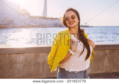 Young stylish woman wearing bright colorful blazer and sunglasses walking on the city street. Casual fashion, fall look. Plus size model.