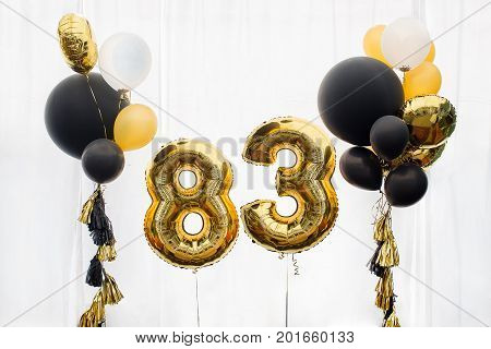 Decoration for birthday, anniversary, celebration of the eighty three anniversary, white background, gold and black balloons with tassels