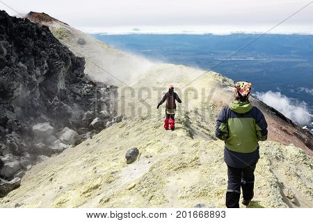 Mountain hiking on Kamchatka Peninsula: two young women tourists walking along sulfur fumarole field in summit crater of active Avacha Volcano on Kamchatka. Eurasia Russian Far East Kamchatka Region