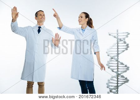 Advanced medicine. Selective focus on a radiant pair of medical workers both wearing white coat smiling while using an invisible touchscreen over the light background.